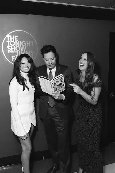 Three smiling people holding a book.