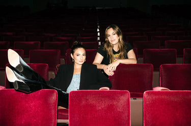 Two women in a movie theater, one with her feet up on a seat.