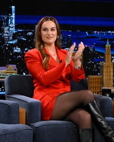 Woman in a red blazer dress, black tights, and black boots, clapping.
